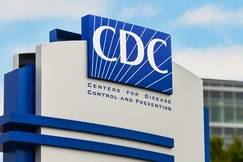 CDC (Centers for Disease Control and Prevention) sign outside headquarters, with blue and white logo against a partly cloudy sky.